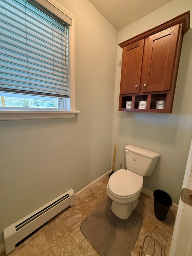 bathroom with a baseboard heating unit, toilet, stone finish floor, and baseboards