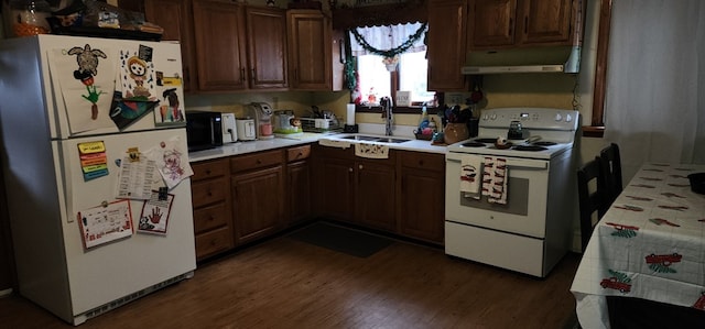 kitchen with white appliances, under cabinet range hood, light countertops, and a sink