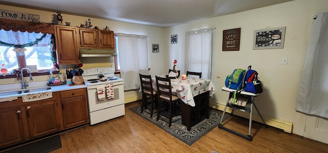 kitchen featuring electric stove, a sink, under cabinet range hood, baseboard heating, and light countertops
