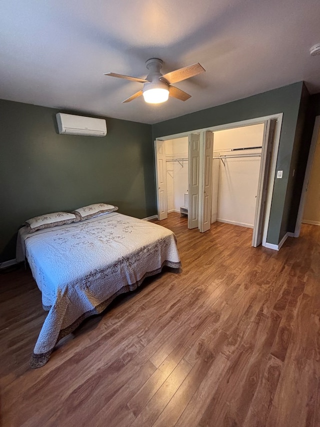 bedroom featuring multiple closets, ceiling fan, a wall mounted air conditioner, and hardwood / wood-style flooring