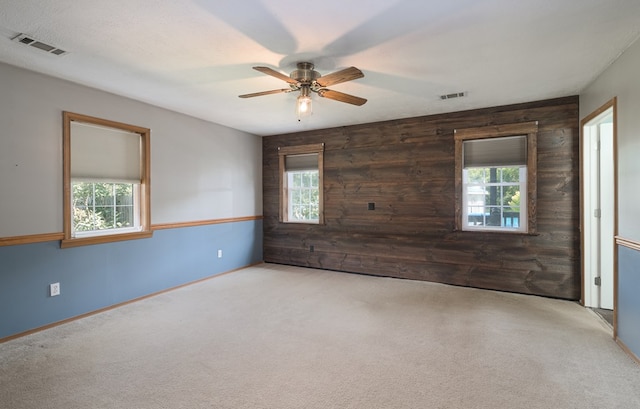 unfurnished room featuring a ceiling fan, carpet floors, wooden walls, and baseboards