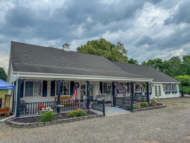 view of front of property with covered porch, roof with shingles, and a chimney