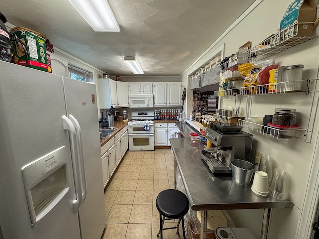 kitchen featuring light tile patterned floors, dark countertops, white cabinets, a sink, and white appliances