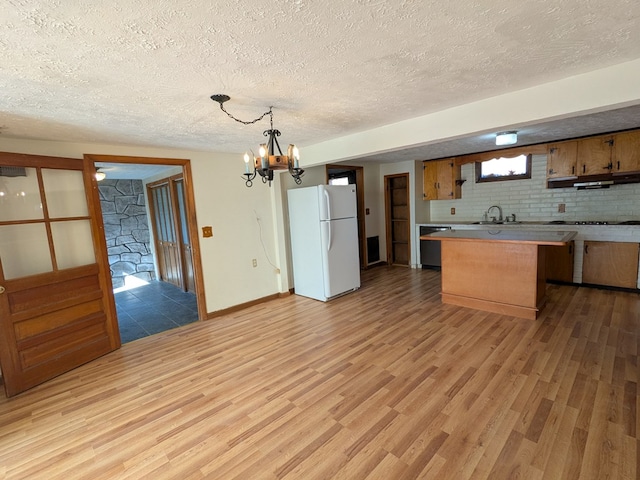 kitchen with dishwashing machine, light wood finished floors, backsplash, and freestanding refrigerator