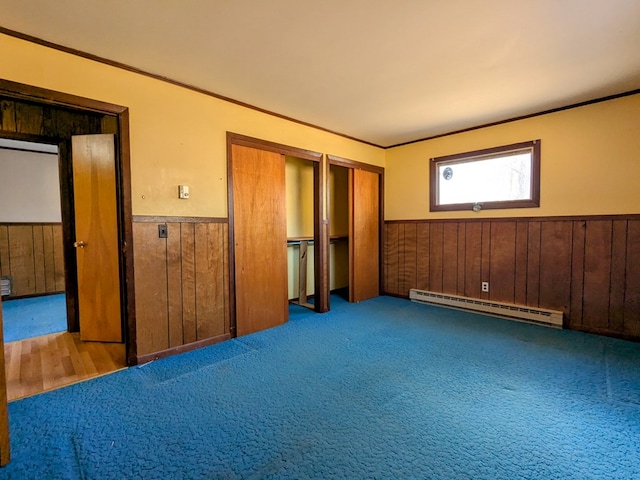 unfurnished bedroom with crown molding, two closets, a baseboard radiator, wainscoting, and wooden walls