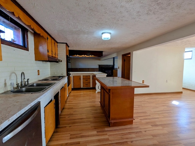 kitchen featuring light wood finished floors, backsplash, brown cabinets, stainless steel dishwasher, and a sink