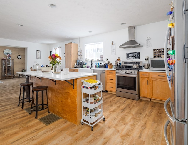 kitchen with wall chimney exhaust hood, stainless steel appliances, a breakfast bar, and light hardwood / wood-style flooring