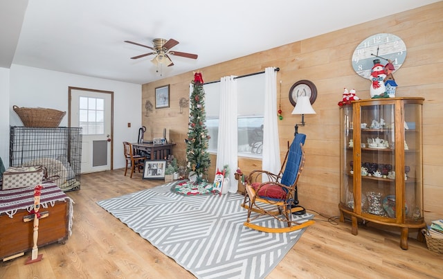 sitting room featuring light hardwood / wood-style flooring, ceiling fan, and wooden walls