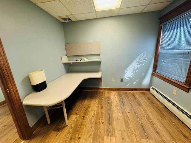 unfurnished office with light hardwood / wood-style flooring, a baseboard radiator, and a drop ceiling