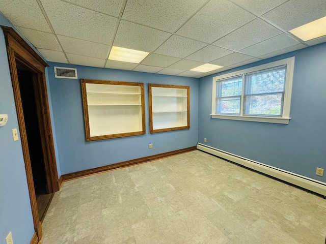 empty room with a drop ceiling, built in shelves, and a baseboard heating unit