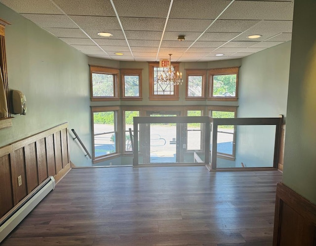 doorway with a paneled ceiling, an inviting chandelier, dark hardwood / wood-style flooring, and a baseboard heating unit