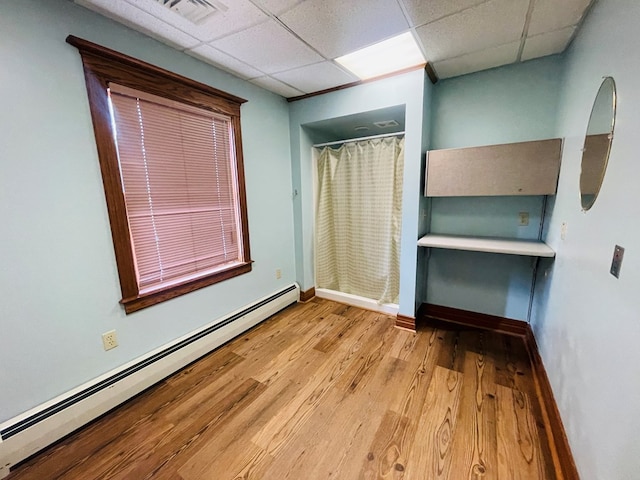 unfurnished bedroom featuring light hardwood / wood-style flooring, a drop ceiling, and a baseboard heating unit