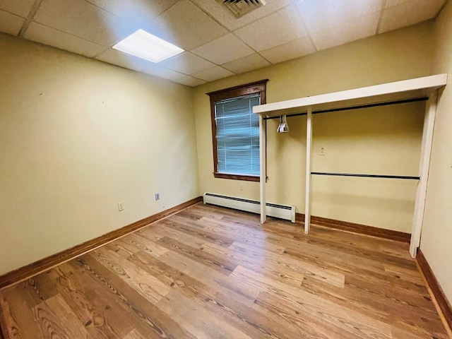 unfurnished bedroom featuring light wood-type flooring, baseboard heating, and a paneled ceiling