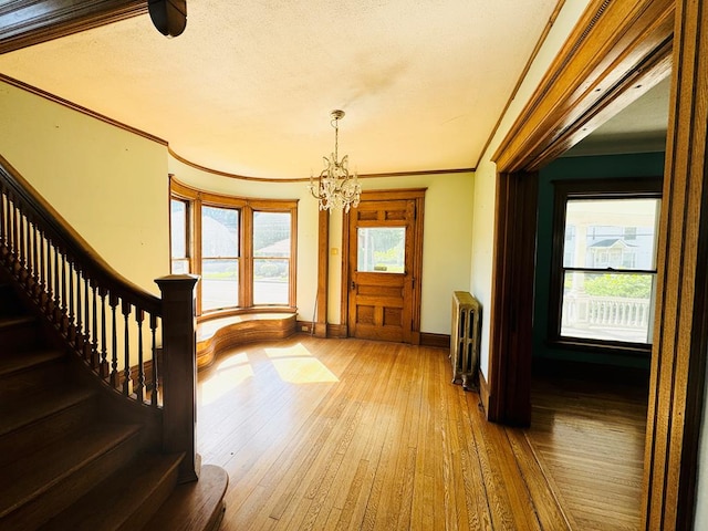 foyer entrance with hardwood / wood-style floors, plenty of natural light, radiator heating unit, and ornamental molding