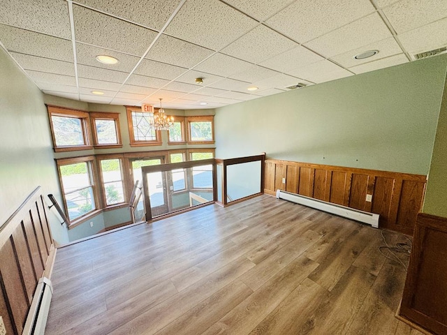 unfurnished room with a paneled ceiling, a notable chandelier, baseboard heating, and hardwood / wood-style flooring