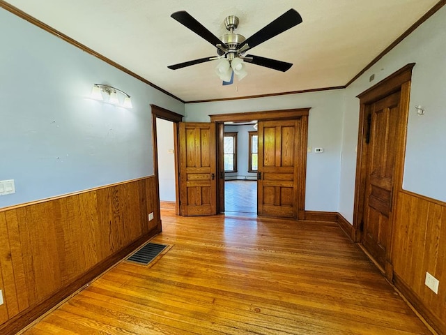 empty room with crown molding, ceiling fan, light hardwood / wood-style floors, and wood walls