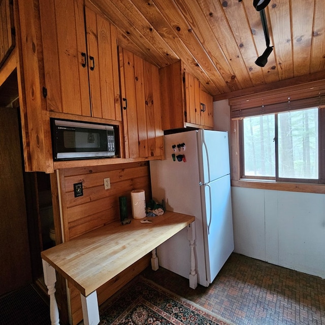 kitchen with wooden ceiling, brown cabinetry, wood walls, and freestanding refrigerator