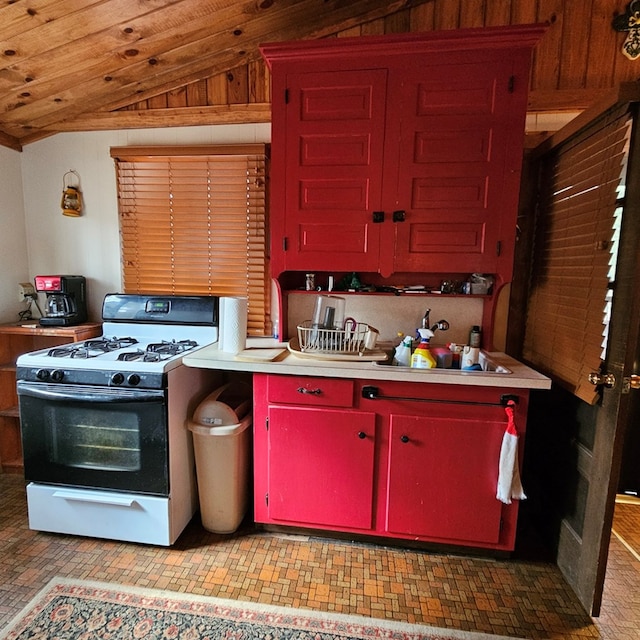 kitchen featuring gas range, red cabinets, light countertops, and lofted ceiling