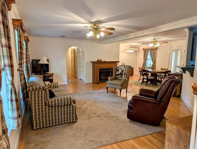 living room featuring a wall mounted air conditioner, crown molding, ceiling fan, and light wood-type flooring