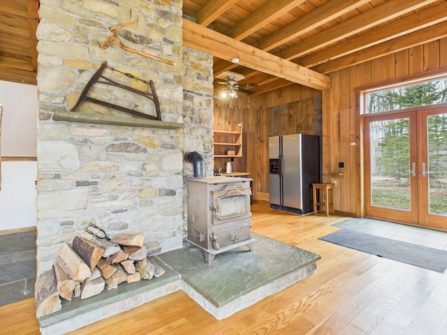 unfurnished living room featuring beamed ceiling, wood ceiling, a wood stove, light wood finished floors, and french doors