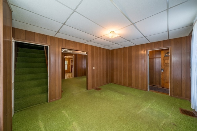 spare room featuring carpet, visible vents, a drop ceiling, and wooden walls