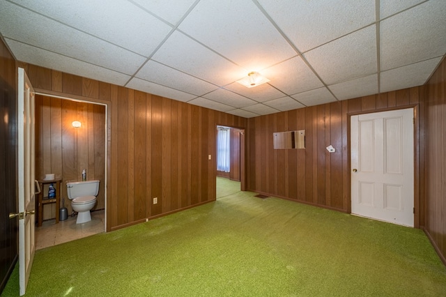 empty room with a paneled ceiling, wooden walls, and light colored carpet