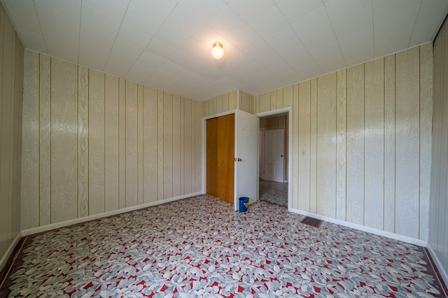 spare room featuring visible vents, wood walls, light carpet, and baseboards