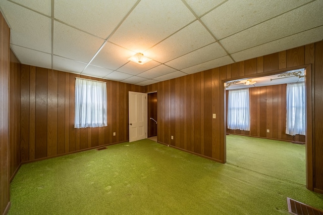 empty room with carpet floors, a paneled ceiling, visible vents, and wooden walls