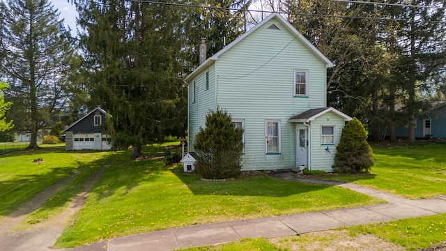 view of side of home featuring driveway, a yard, a chimney, and an outdoor structure