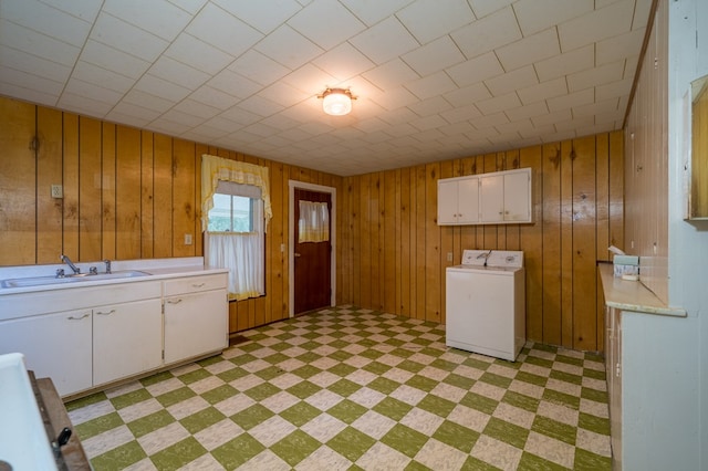 laundry room featuring wood walls, a sink, cabinet space, light floors, and washer / dryer