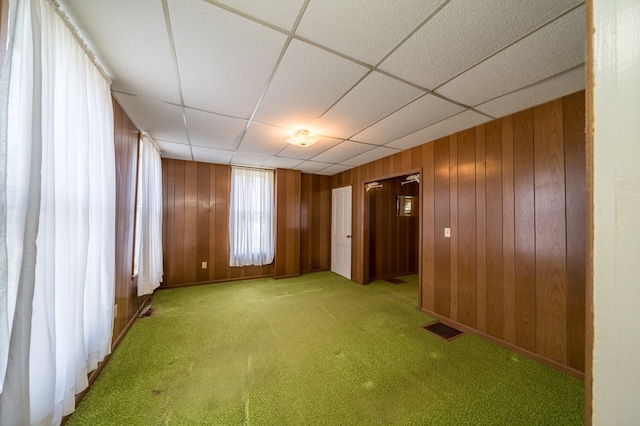 unfurnished room featuring light carpet, wooden walls, visible vents, and a paneled ceiling