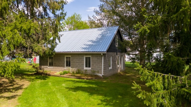 rear view of house featuring concrete block siding, metal roof, and a lawn