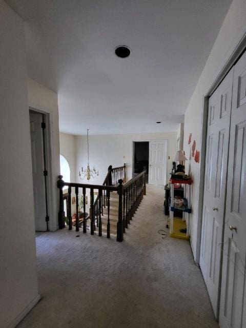 corridor with light colored carpet and an inviting chandelier