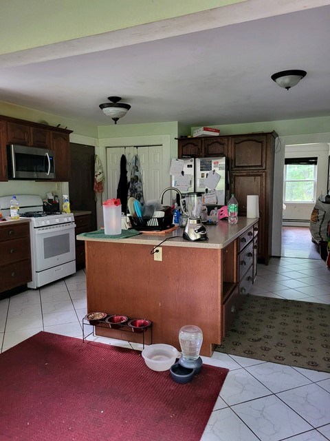 kitchen with dark brown cabinetry, light tile patterned floors, a kitchen island, and white appliances