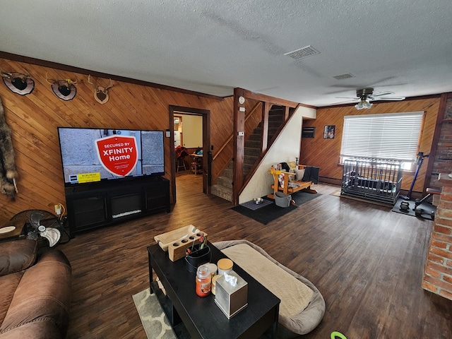 living room with ceiling fan, dark wood-type flooring, wooden walls, and a textured ceiling