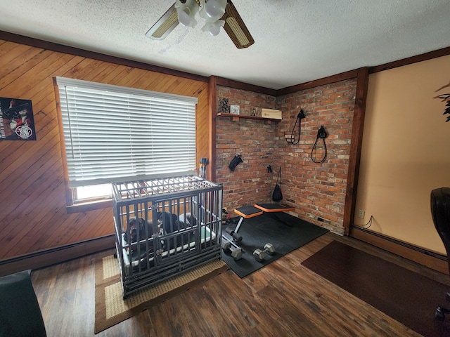 exercise room featuring wood walls, a textured ceiling, hardwood / wood-style flooring, ceiling fan, and brick wall