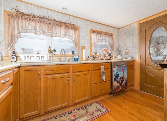 kitchen with a sink, light countertops, light wood finished floors, crown molding, and brown cabinetry