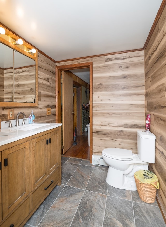 bathroom with stone tile floors, toilet, wooden walls, vanity, and ornamental molding