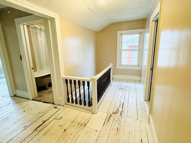 hallway featuring a textured ceiling, light hardwood / wood-style floors, and vaulted ceiling