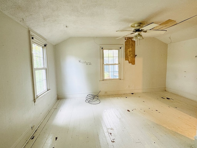 empty room featuring ceiling fan, light wood-type flooring, a textured ceiling, and vaulted ceiling