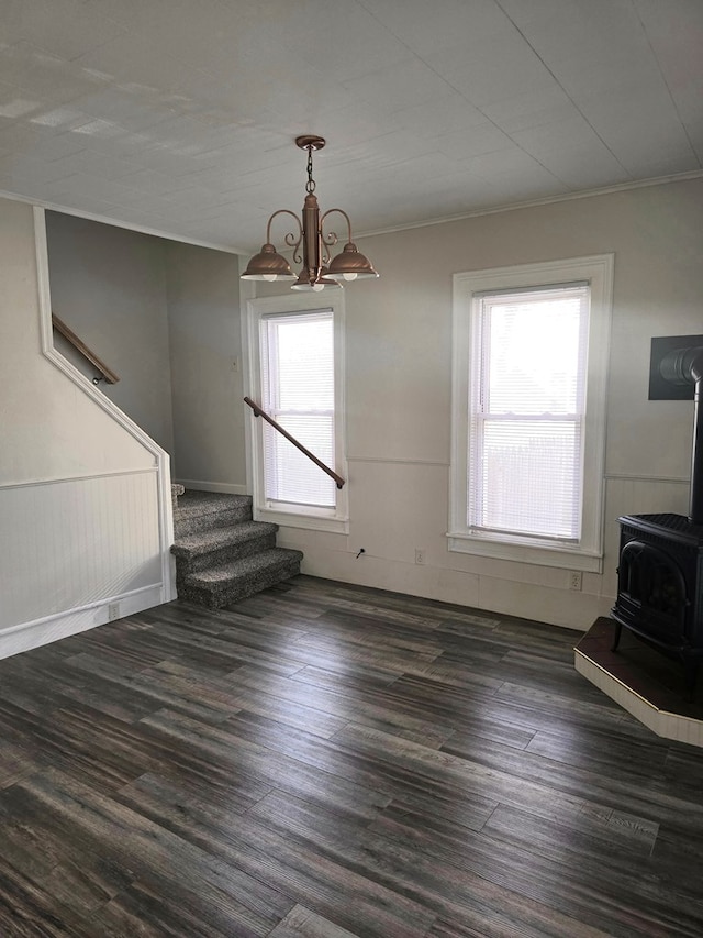 526 Stevenson St, Sayre, PA 18840 - unfurnished living room with a notable chandelier, a wainscoted wall, a wood stove, dark wood-type flooring, and stairs