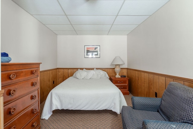 carpeted bedroom with wooden walls and a paneled ceiling