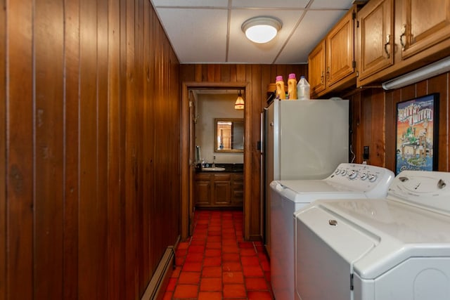 washroom featuring baseboard heating, cabinets, wooden walls, and washing machine and clothes dryer