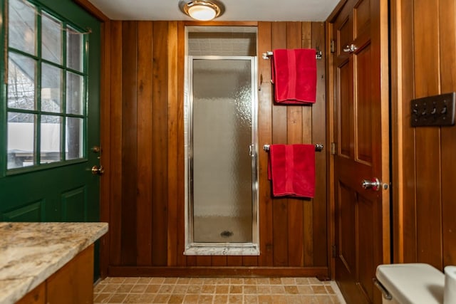 bathroom featuring a shower with door, vanity, wooden walls, and toilet