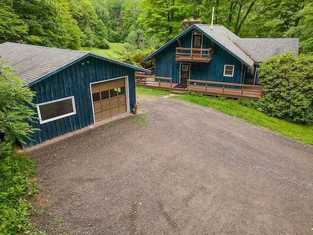 view of front of home with a shingled roof, dirt driveway, a chimney, a balcony, and an outbuilding