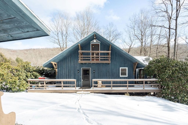 snow covered rear of property featuring a wooden deck and a balcony