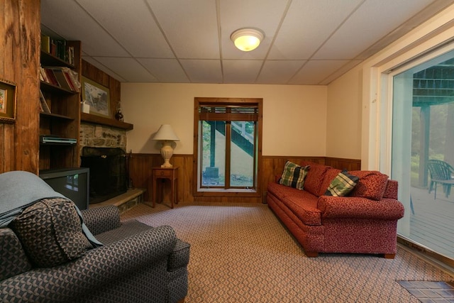 carpeted living room featuring a fireplace, a paneled ceiling, and wood walls