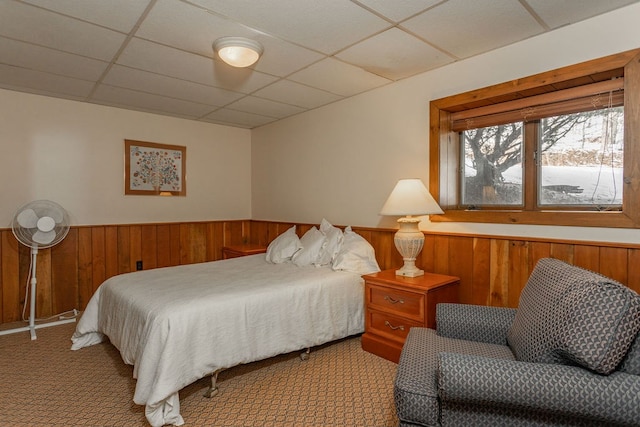 bedroom featuring a wainscoted wall, light colored carpet, a paneled ceiling, and wooden walls