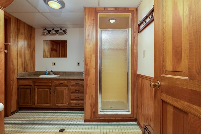 bathroom featuring an enclosed shower, a paneled ceiling, vanity, wooden walls, and a baseboard heating unit