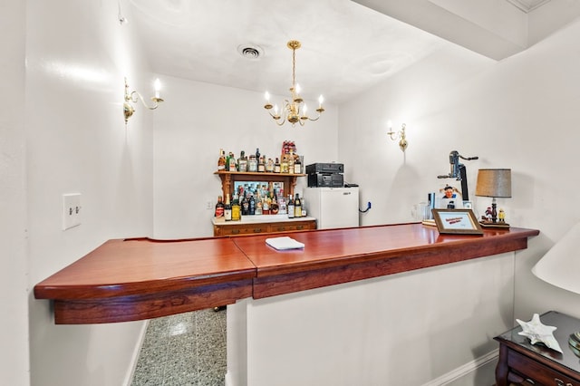 bar with a chandelier, refrigerator, and pendant lighting